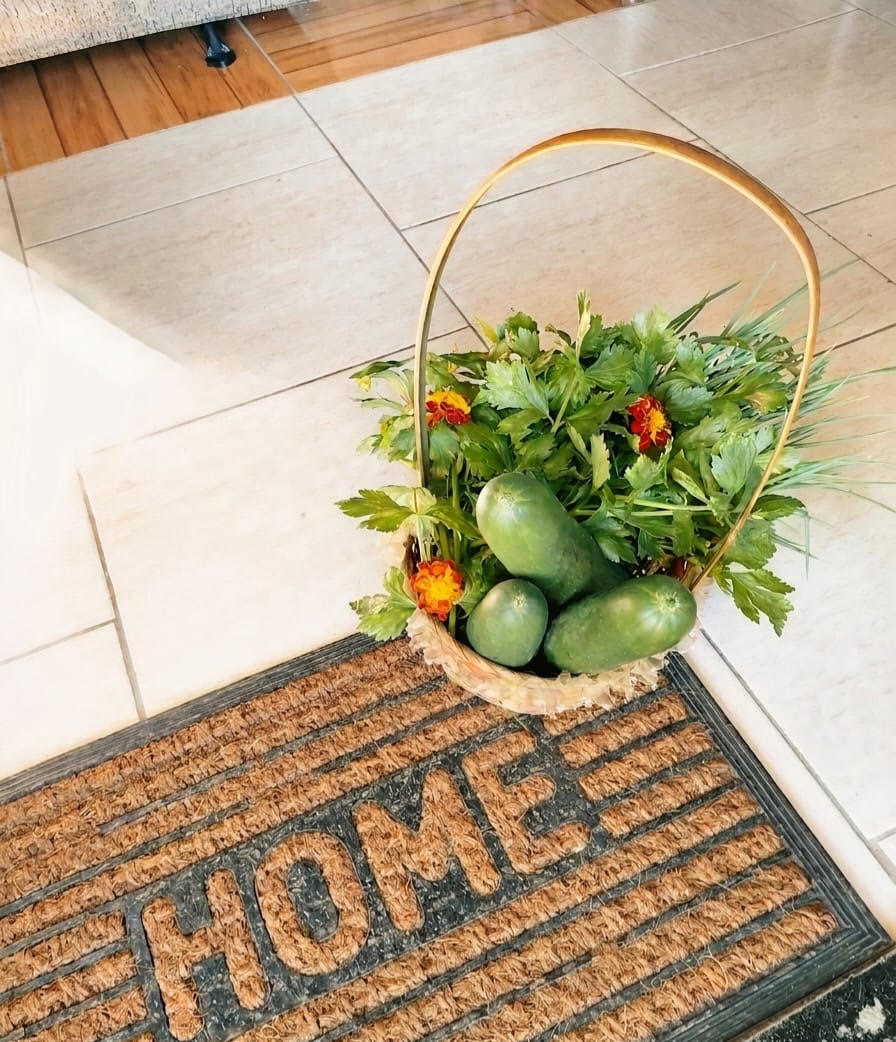 A basket of freshly picked garden produce and marigolds resting on a doormat that reads HOME
